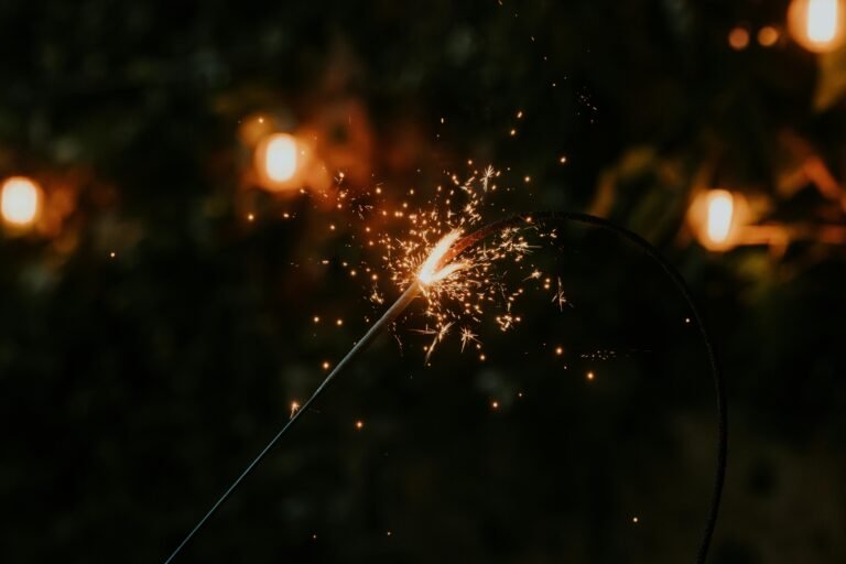 A close-up of a sparkler glowing amid warm, bokeh lights in a dark setting.